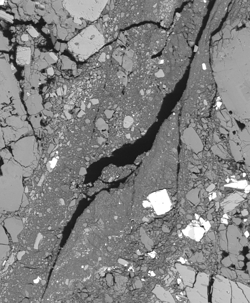 Backscattered scanning electron microscope image of andesite from the Kumamoto prefecture in Kyūshū, Japan. Void space appears as black within a grey groundmass interspersed by dense, metal-rich crystals which appear as light-grey or white. This sample has been experimentally fractured and has undergone large amounts of strain—volumetric change—in order to replicate progressive mechanical deformation in a volcanic setting. Comminuted granular material is abundant within the fracture, with pulverized phenocrysts highlighting significant shear on the fault.  